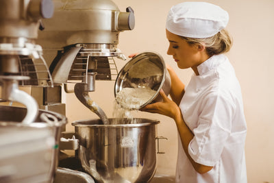 Chef adding flour into a stainless-steel spiral mixer