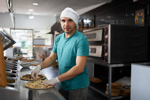 A chef making pizza on a pizza prep fridge